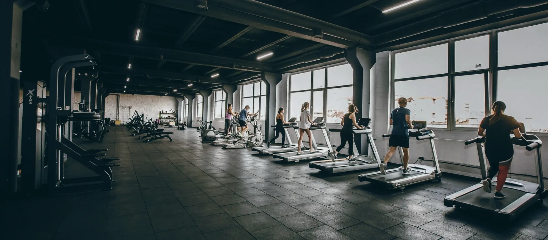 Простора зала FitMe — ряд бігових доріжок до високих панорамних вікон, учасники тренуються у нічному світлі